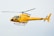 A bright yellow helicopter is flying in the sky, showcasing sleek aerodynamic design with visible registration marks. The helicopter has a single main rotor and a tail rotor.