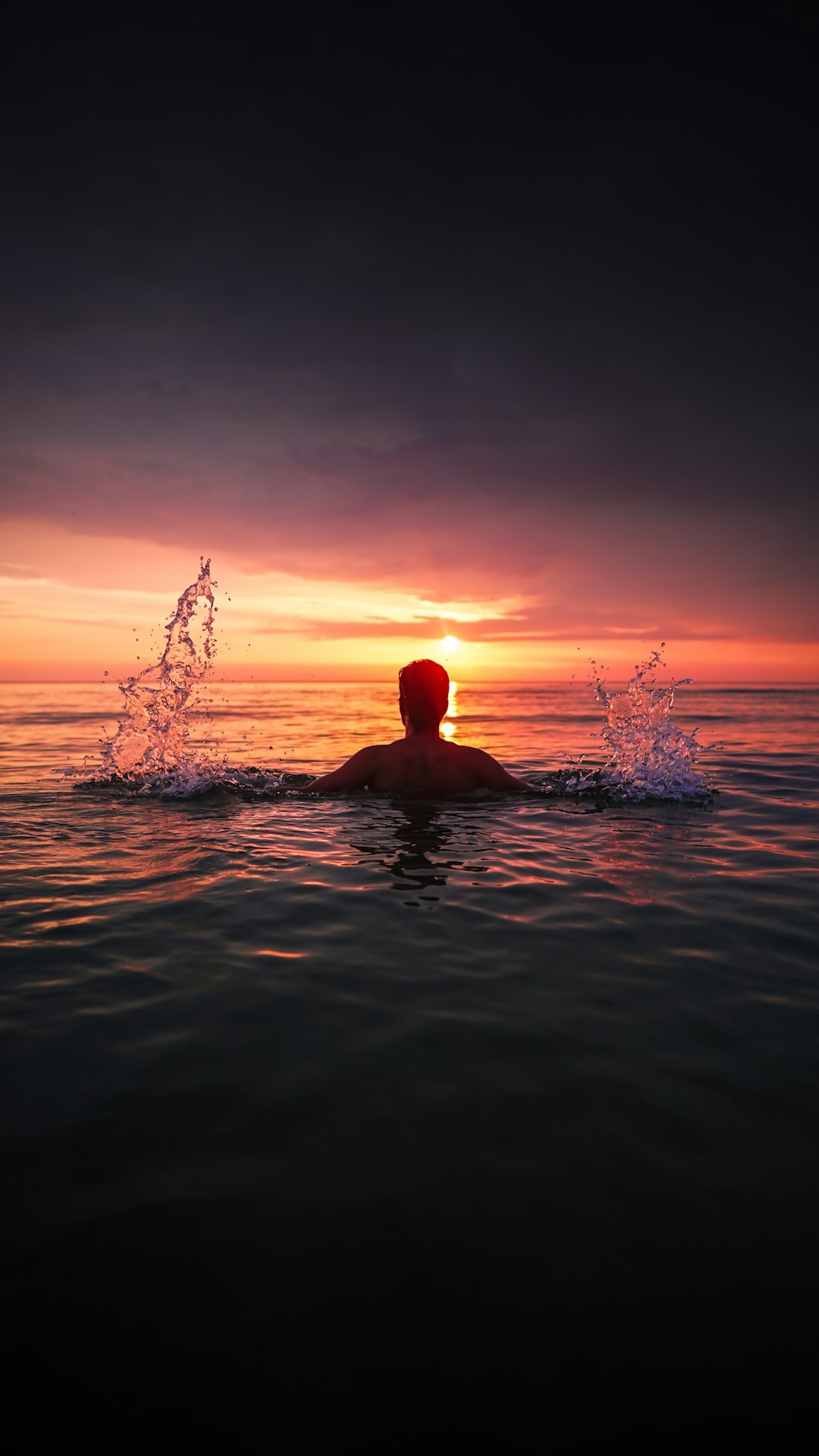 a man swimming in the ocean at sunset