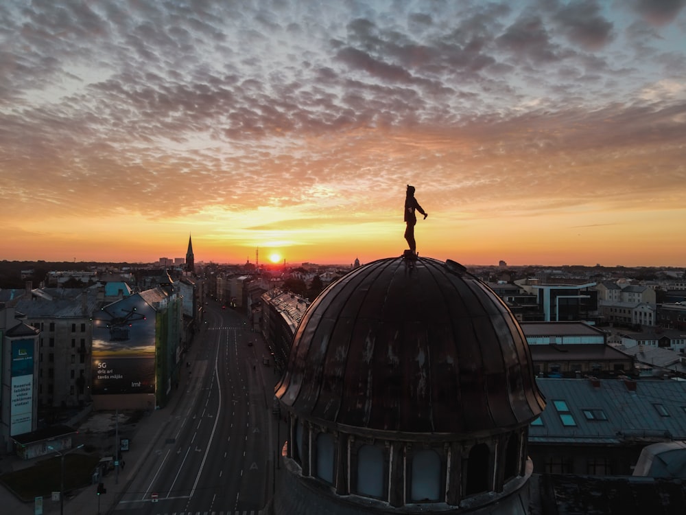eine Person, die auf dem Dach eines Gebäudes mit einem Sonnenuntergang im Hintergrund steht