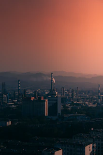A vintage industrial skyline at dusk, with smokestacks silhouetted against a deep rust-colored sky.