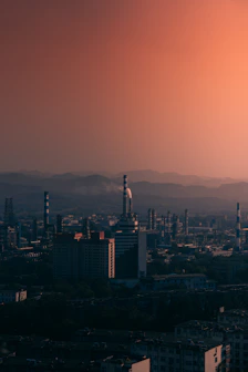 A vintage industrial skyline at dusk, with smokestacks silhouetted against a deep rust-colored sky.