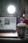 A cozy workspace with a laptop displaying an out-of-focus screen, a smartphone showing the time, and a branded coffee cup in the foreground. A bright light source illuminates the scene from behind the laptop.