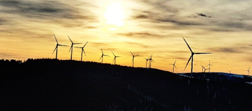 Wind turbines spinning on a hill at sunset with orange and gray skies