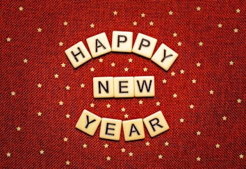 Scrabble tiles spell out the words 'Happy New Year' on a red background with scattered small gold stars.