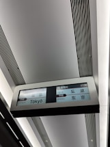 An electronic display sign inside a station shows travel information in multiple languages. It indicates a train arriving at Tokyo, with the label '10 NEX' and the time 21:38 clearly visible.