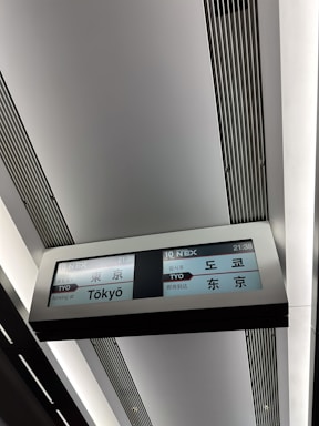 An electronic display sign inside a station shows travel information in multiple languages. It indicates a train arriving at Tokyo, with the label '10 NEX' and the time 21:38 clearly visible.