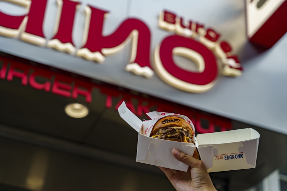 a person holding a box of food in front of a fast food restaurant