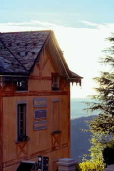 A charming building with rustic architecture, featuring a weathered roof and ornate wooden details. The signs on the exterior read 'Bellavista' and 'Ristorante Bar'. The structure is set against a backdrop of a scenic landscape with trees and a distant horizon under a bright sky.