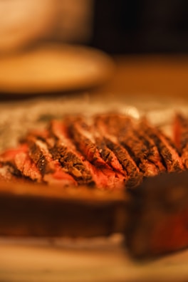 Chef carefully slicing a dry-aged beef cut in a dimly lit kitchen with warm beige lighting.