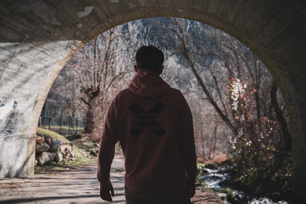 a man in a red sweatshirt is walking under a bridge