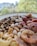 A plate filled with an assortment of mixed nuts and dried fruits including cashews, pistachios, chickpeas, dates, and dried figs. The background is blurred, featuring greenery and distant buildings.
