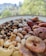 A plate filled with an assortment of mixed nuts and dried fruits including cashews, pistachios, chickpeas, dates, and dried figs. The background is blurred, featuring greenery and distant buildings.