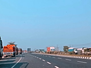 A fleet of trucks lined up on a highway under a clear blue sky.