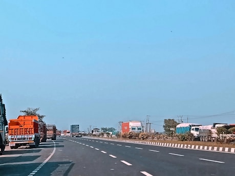 A fleet of trucks lined up on a highway under a clear blue sky.