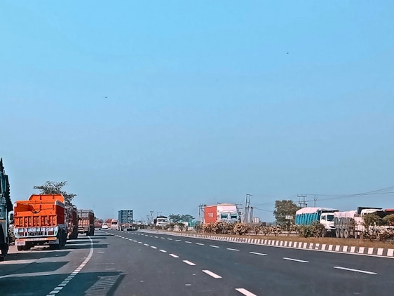 A fleet of trucks on a highway surrounded by lush green landscapes under a clear blue sky.