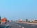 An empty highway stretches into the distance under a clear blue sky, with multiple colorful trucks parked along the side. Sparse greenery and utility poles line the road, giving the scene a sense of stillness.