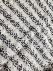 A close-up view of a knitted fabric with a textured pattern featuring diagonal zigzag stripes in dark brown on a cream background.