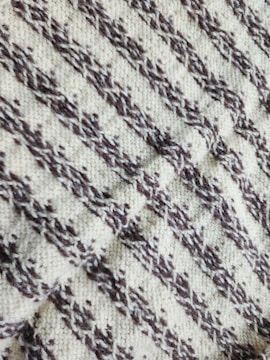 A close-up view of a knitted fabric with a textured pattern featuring diagonal zigzag stripes in dark brown on a cream background.