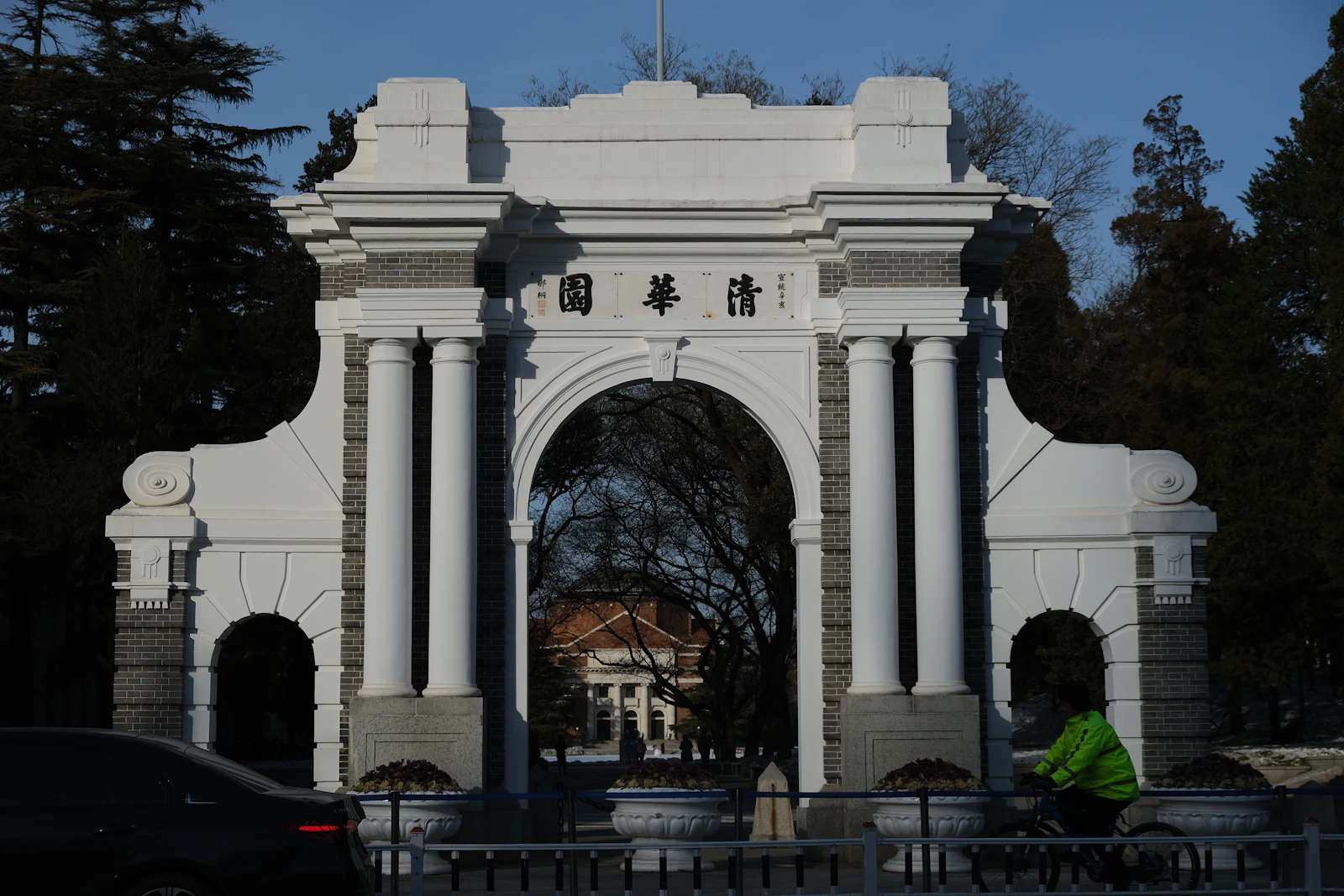 Cyclist passing the white arch of Tsinghua University's old gate in snow, Beijing, China