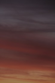 A horizon filled with gradient colors transitioning from deep orange and red to darker shades of blue and grey, resembling a sunset or sunrise.