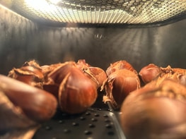 Artisan gently hand-roasting almonds over a small flame in a copper pan.