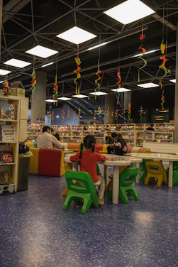 A vibrant scene of children eagerly reading books inside a colorful mobile library van in a serene village setting.