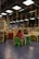 A library or reading area with colorful seating arrangements is filled with children and adults. The ceiling features hanging decorative spirals in various colors. Bookshelves and tables are scattered around, with people engaging in reading or activities.