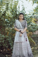 A model wearing a flowing Afghan dress with delicate patterns, standing in a sunlit garden.