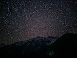 A dark, star-studded sky over a shadowed mountain range with faint glowing constellations.