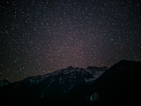 A dark, star-studded sky over a shadowed mountain range with faint glowing constellations.