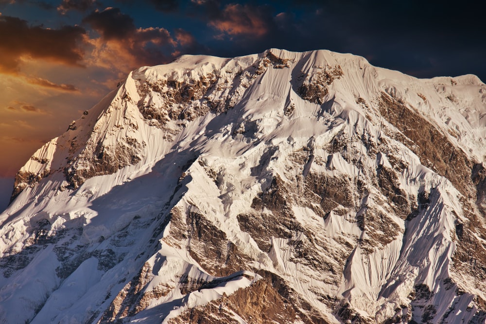 a mountain covered in snow under a cloudy sky