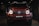 A red, powerful SUV with distinctive front headlights is displayed in a dimly lit showroom setting. The vehicle features a prominent grille with a recognizable emblem at the center and has a sleek, modern design that underscores its luxury and performance attributes.