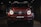 A red, powerful SUV with distinctive front headlights is displayed in a dimly lit showroom setting. The vehicle features a prominent grille with a recognizable emblem at the center and has a sleek, modern design that underscores its luxury and performance attributes.