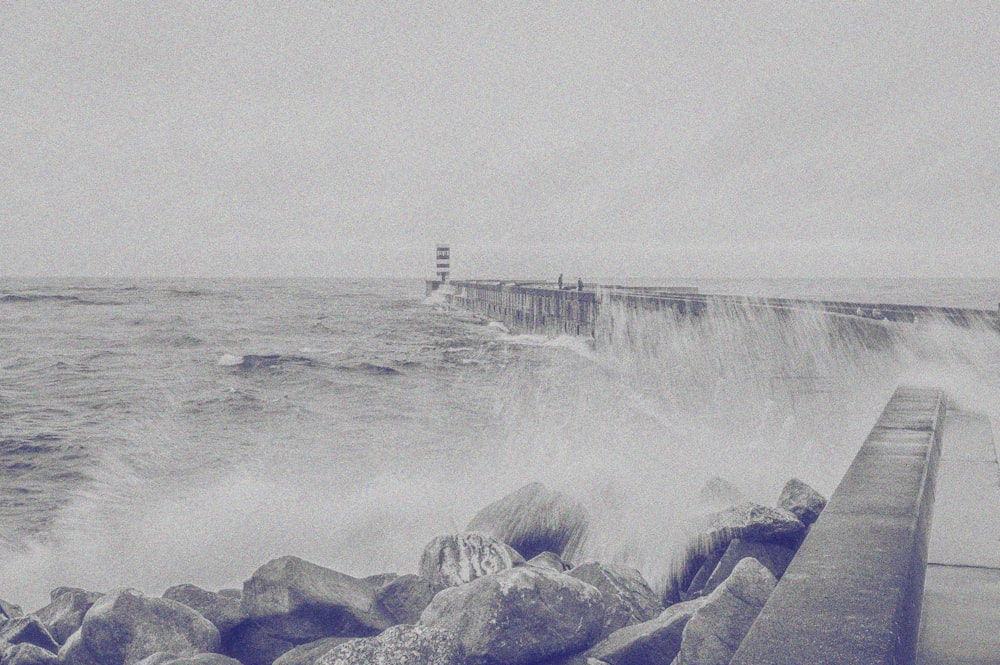 a black and white photo of waves crashing on a pier