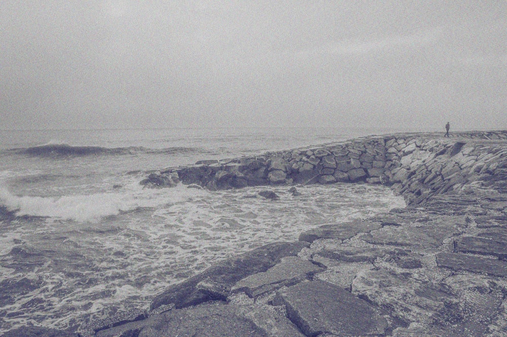 a black and white photo of a person standing on a rocky shore