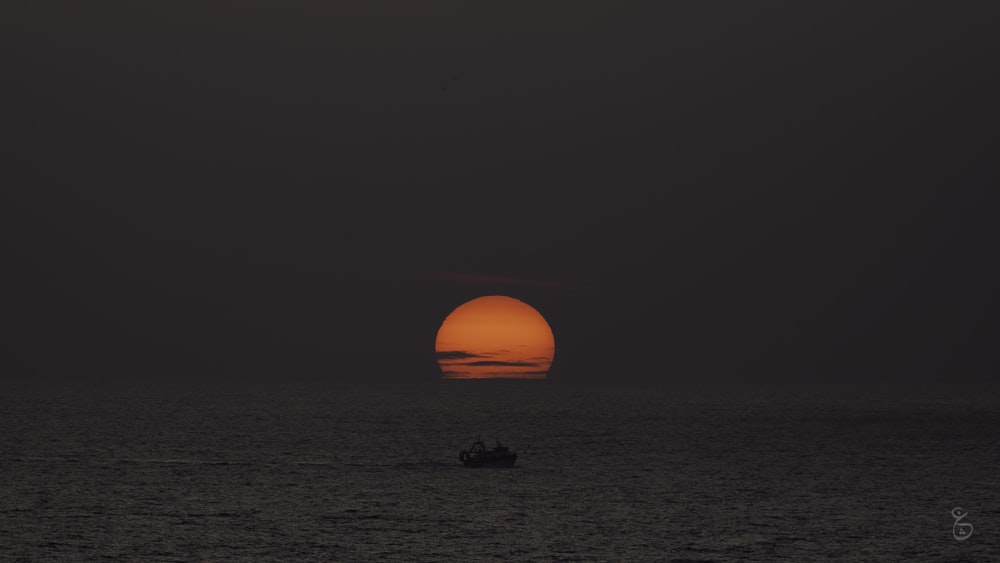 a boat in the ocean with the sun setting in the background