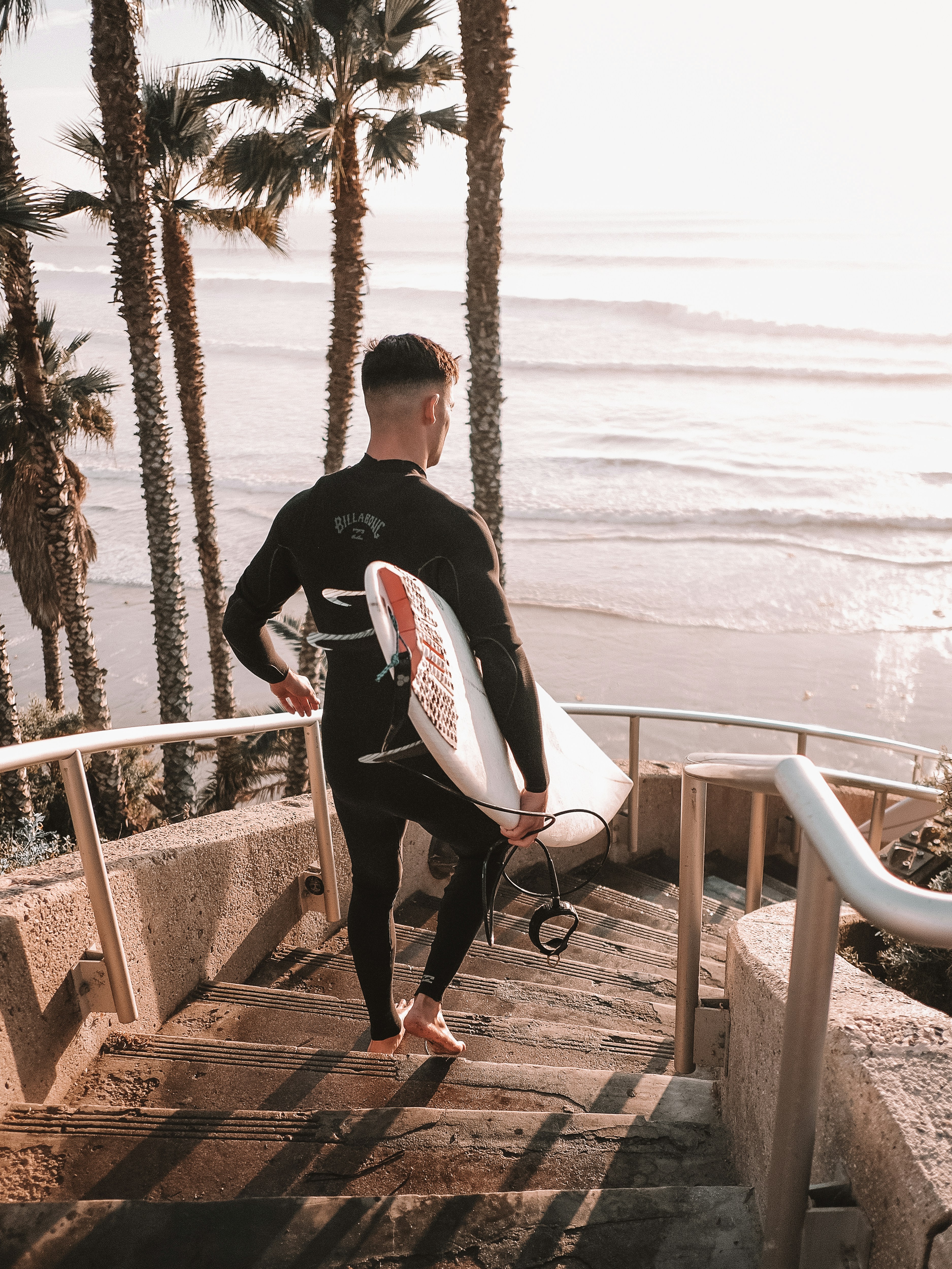 Un homme en combinaison de plongée transportant une planche de surf dans un escalier