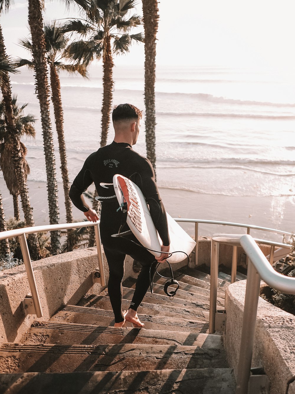 a man in a wet suit carrying a surfboard down a flight of stairs