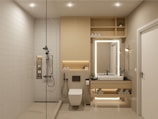 A modern, minimalistic bathroom featuring a walk-in shower with a rain shower head, a built-in shelf with toiletries, and a floating vanity with backlit mirror. The space includes a wall-mounted toilet, neatly stacked towels, potted plants, and recessed ceiling lights for a clean and organized look.