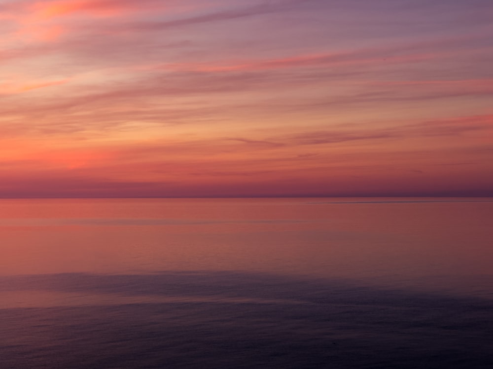 a sunset over the ocean with a boat in the water