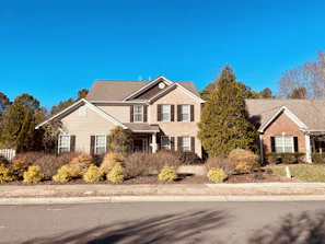 A cozy suburban house with a welcoming front porch and blooming garden under a clear blue sky