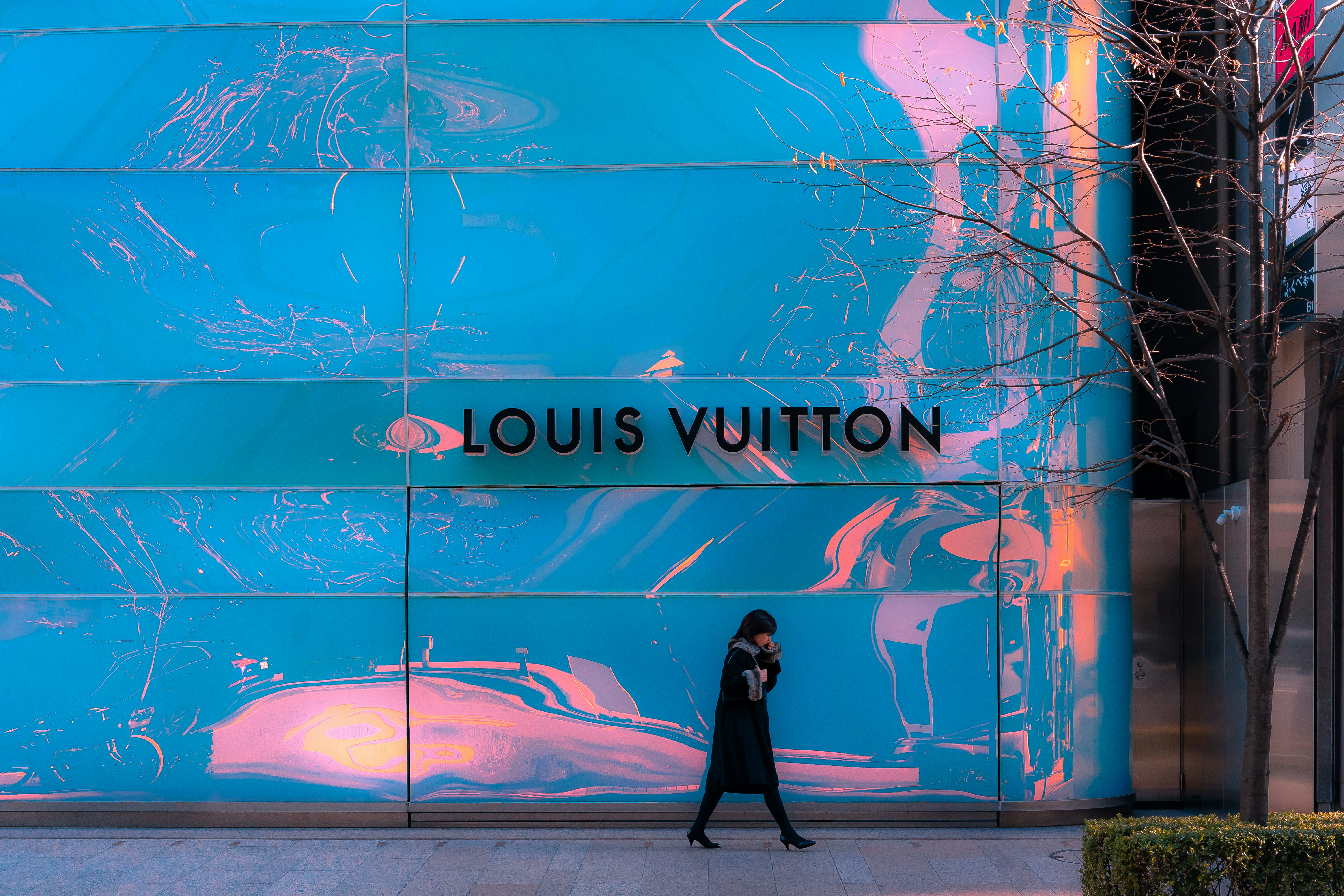 a woman walks past a louis vuitton store