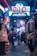 A bustling shopping arcade illuminated with bright neon signs. Various clothing items are displayed on racks lining the narrow walkway. A person in a blue jacket and skirt stands by a sale sign, while several other people mill about, browsing and chatting.