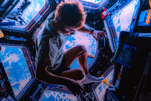 An individual is floating in a spacecraft, surrounded by multiple circular windows offering a stunning view of the Earth below. The scene is filled with various devices and equipment typically found inside a space station.