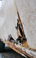 A close-up view of a severely rusted and peeling section of a vehicle's body panel, showing exposed metal and corrosion.