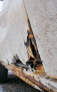 A close-up view of a severely rusted and peeling section of a vehicle's body panel, showing exposed metal and corrosion.