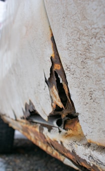 A close-up view of a severely rusted and peeling section of a vehicle's body panel, showing exposed metal and corrosion.