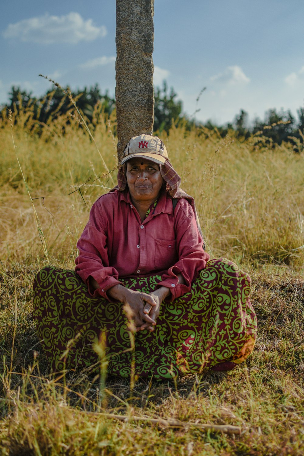 a woman sitting under a tree in a field