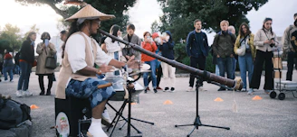 A colorful didgeridoo player smiling warmly during an outdoor music event.