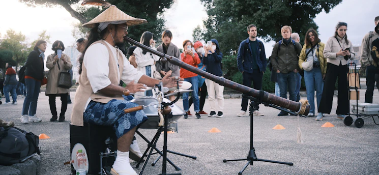 A colorful didgeridoo player smiling warmly during an outdoor music event.